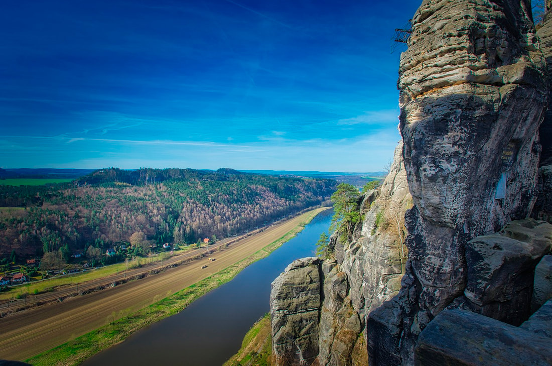 Sandstone cliffs overlooking the Elbe River and railway tracks below. Image by xMaster from Pixabay.